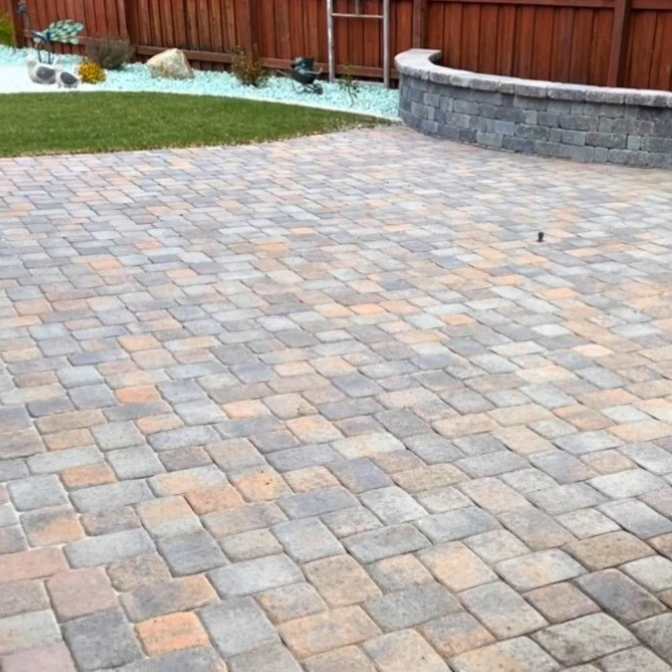 Completed multicolor paver patio bordered by a curved block wall