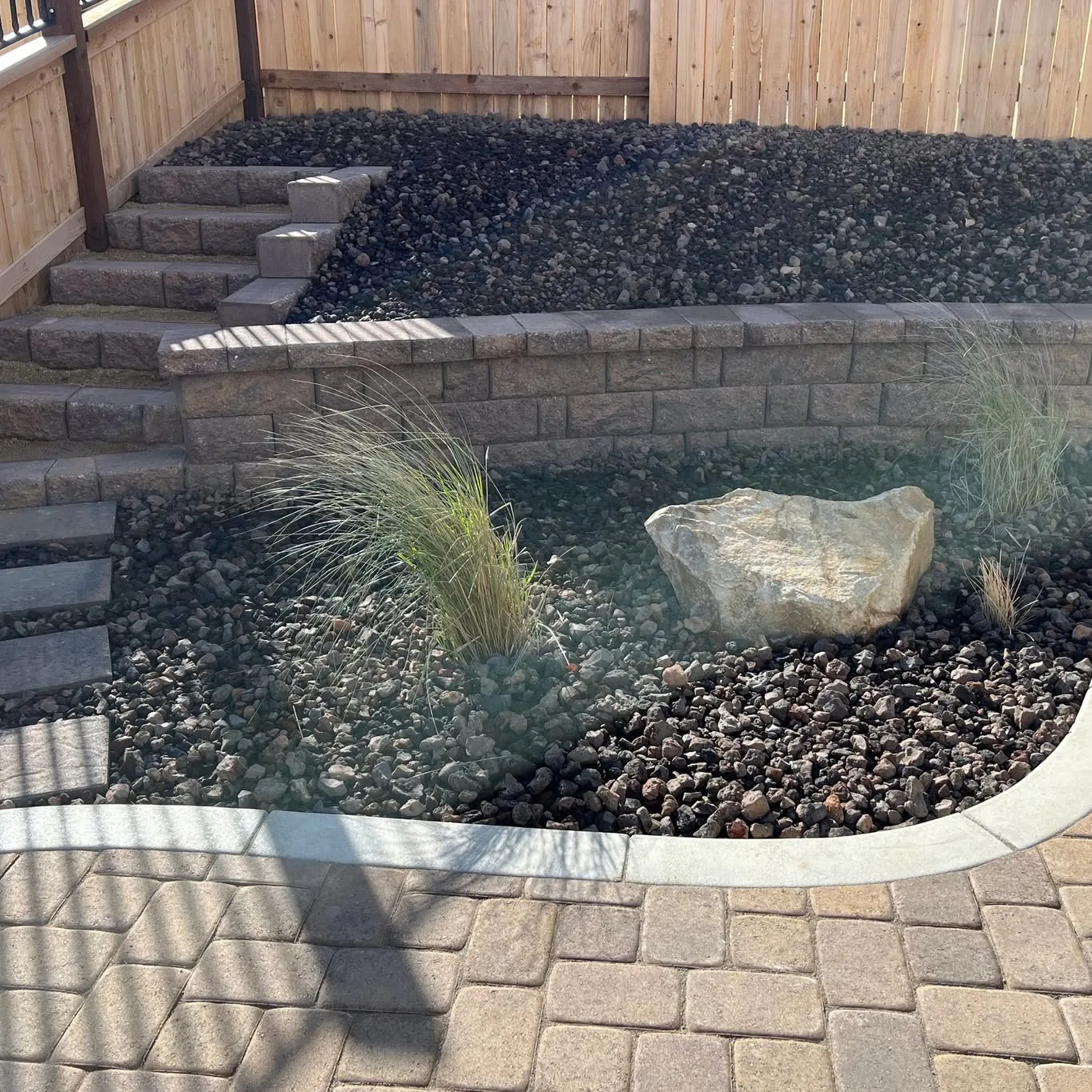 Paver pattern beside retaining-wall block, decorative rock, and ornamental grasses