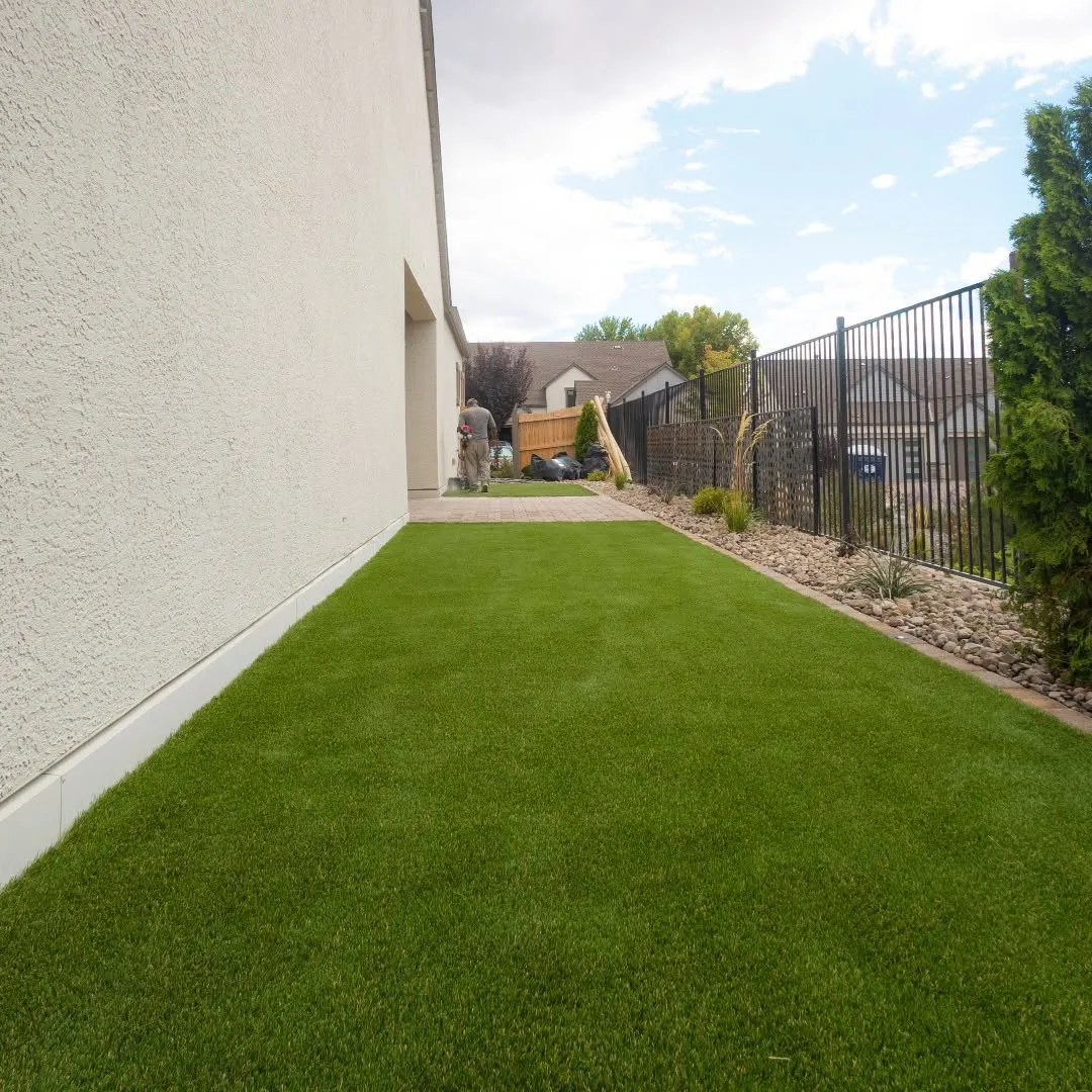 Completed artificial-turf side yard beside a paver walkway and landscaped rock bed